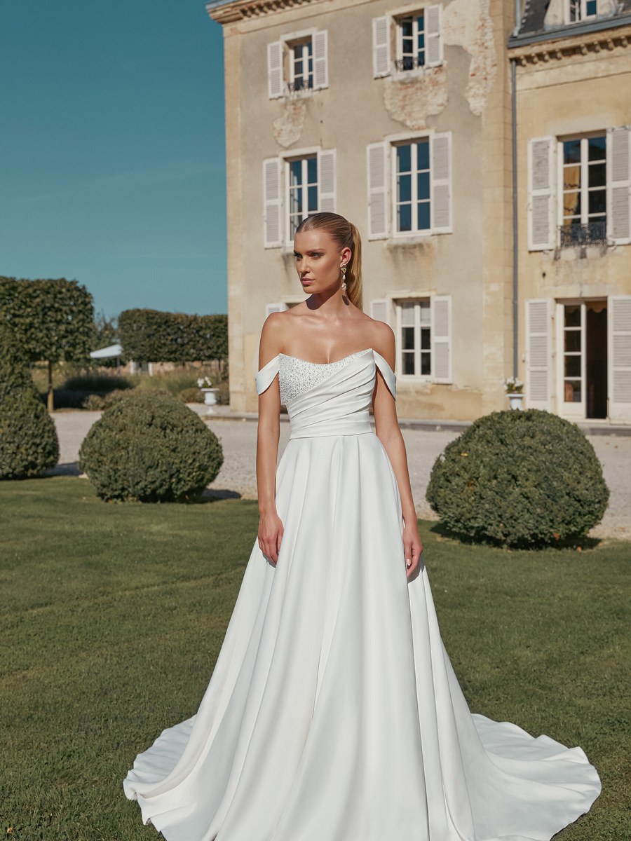 Off-shoulder satin A-line gown before a stone chateau
